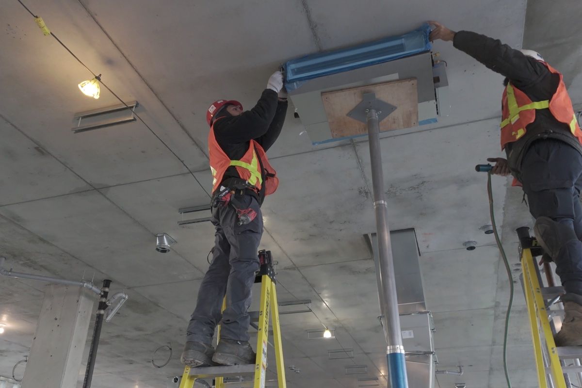 Deux techniciens de Solutions Controlium installant une unité au plafond sur des échelles